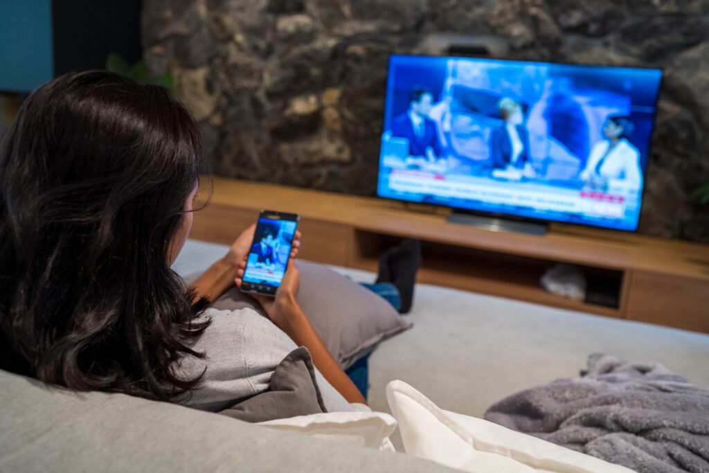 Young woman watching news on television and smart phone