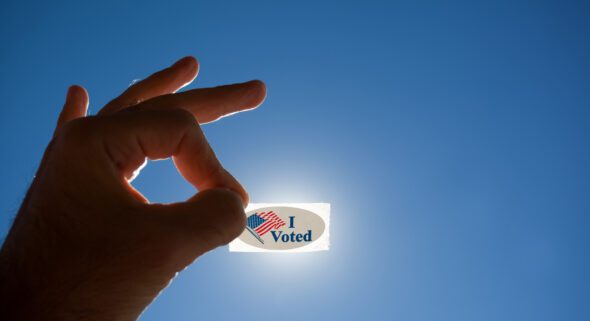 Voter holding up an "I Voted" sticker at a polling location.