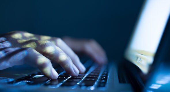 Close up image of a person typing in the dark on their laptop