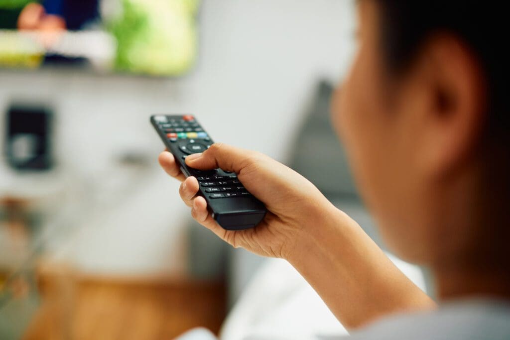 Close-up of woman changing channels on TV at home.