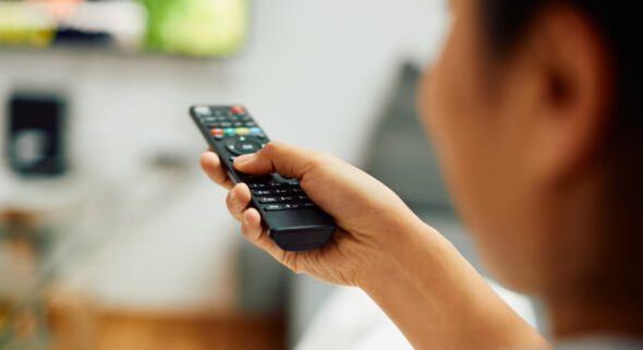 Close-up of woman changing channels on TV at home.